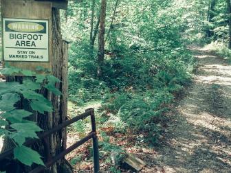 Warning Bigfoot Area Stay on Marked Trails Sign on Tree on Vermont Dirt road with gate.
